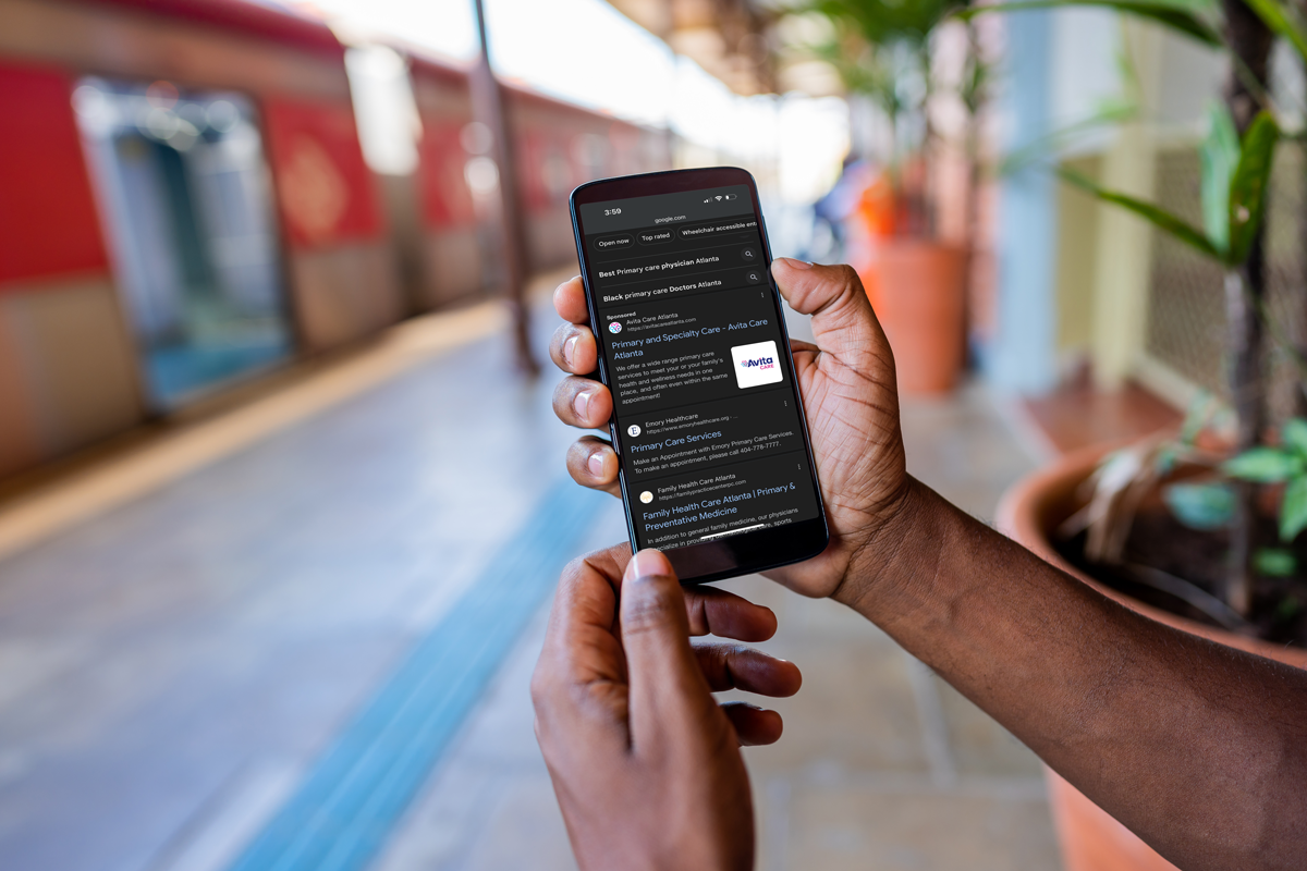 Close-up of a person holding a smartphone displaying Google search results for primary care services in Atlanta, featuring an ad for AvitaCare Atlanta.